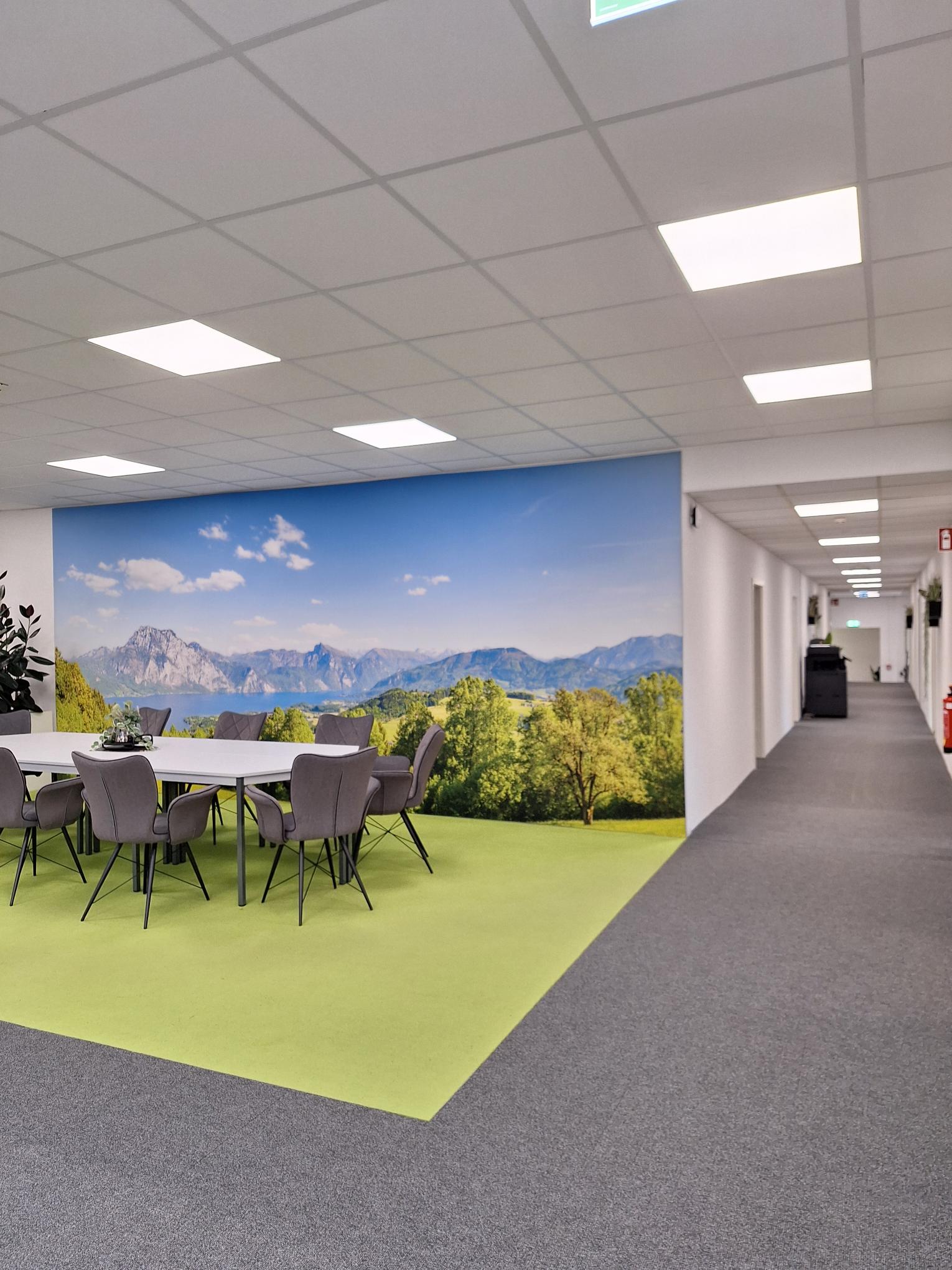 ein Zimmer mit Stühlen und einem großen Tisch, Pflanzen und einem großen Foto einer Landschaft